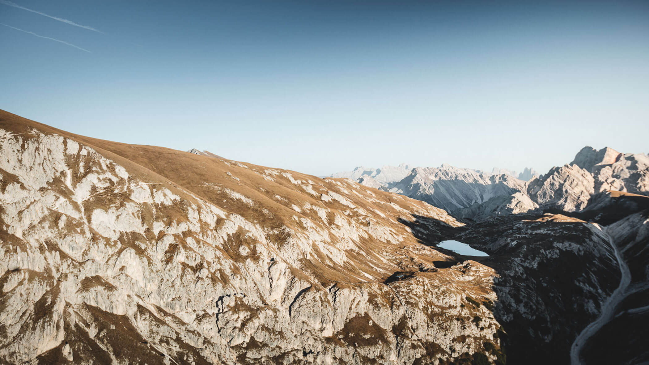 Mountain landscape with rocky slopes, a narrow lake, and distant peaks under a clear blue sky. - Pension Pfarrwirt
