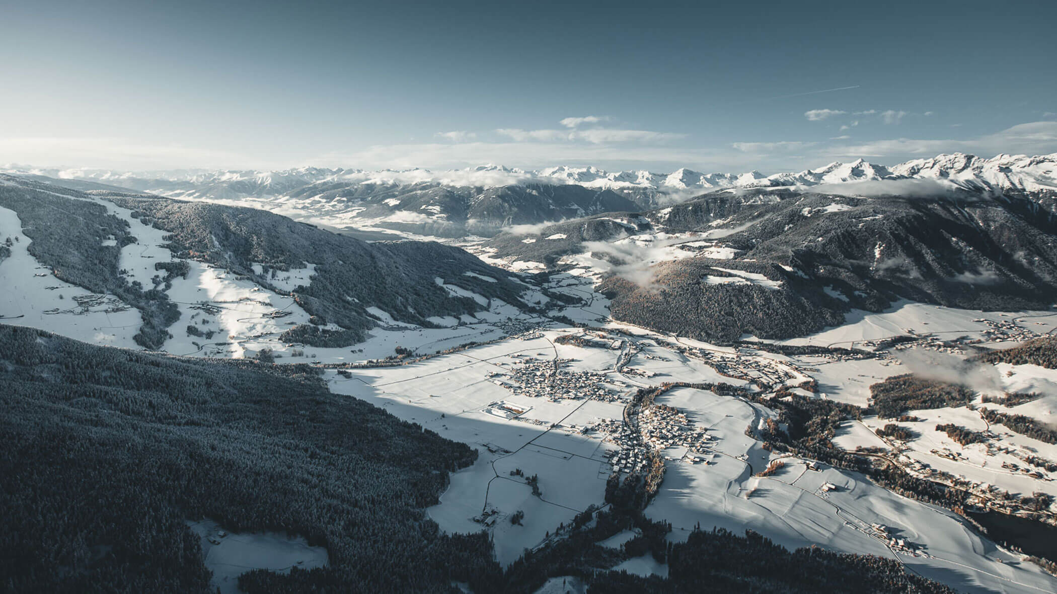 Aerial view of a snow-covered mountain village surrounded by forested hills and distant peaks. - Pension Pfarrwirt