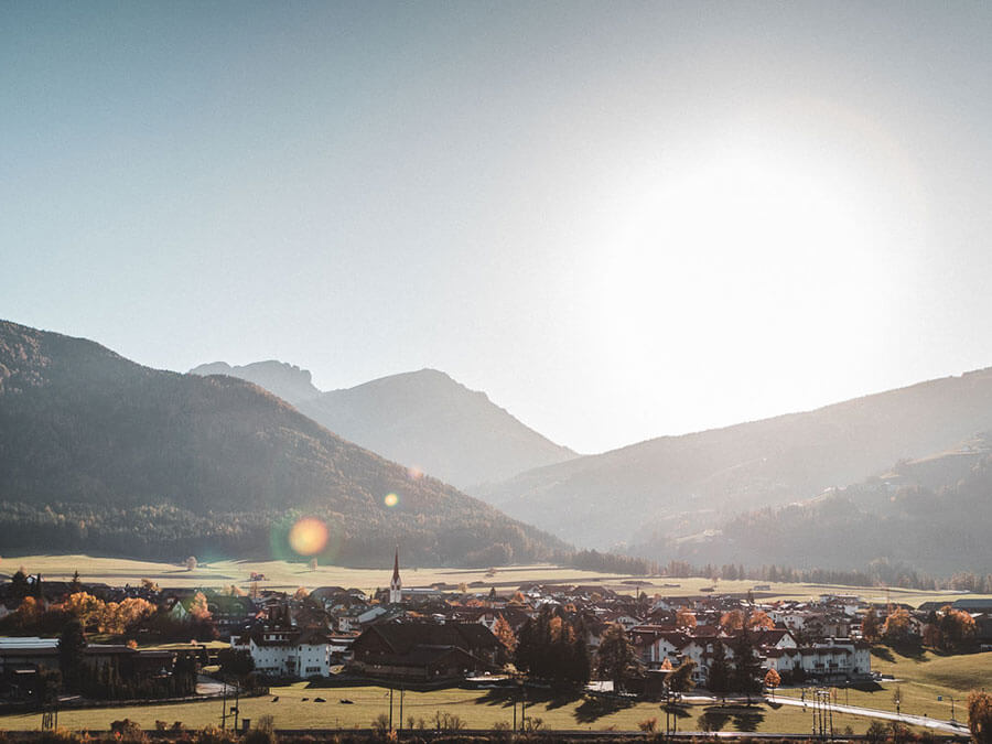 Small village nestled in a valley with mountains in the background and the sun shining brightly overhead. - Pension Pfarrwirt